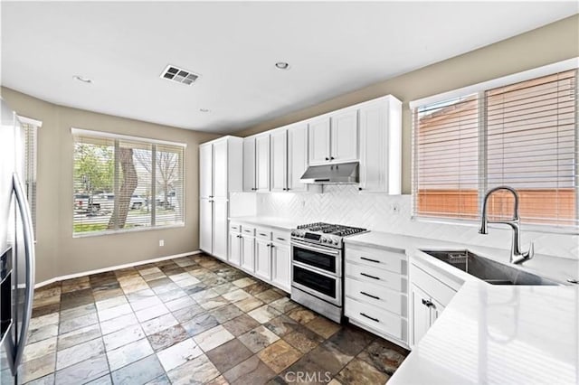 kitchen with under cabinet range hood, visible vents, a sink, tasteful backsplash, and appliances with stainless steel finishes