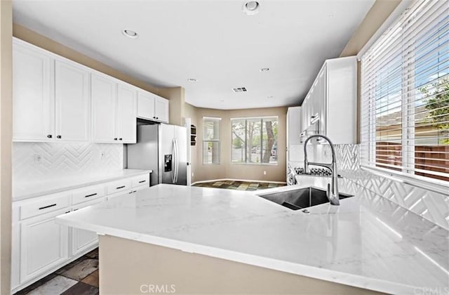 kitchen with a peninsula, a sink, stainless steel fridge with ice dispenser, backsplash, and light stone counters