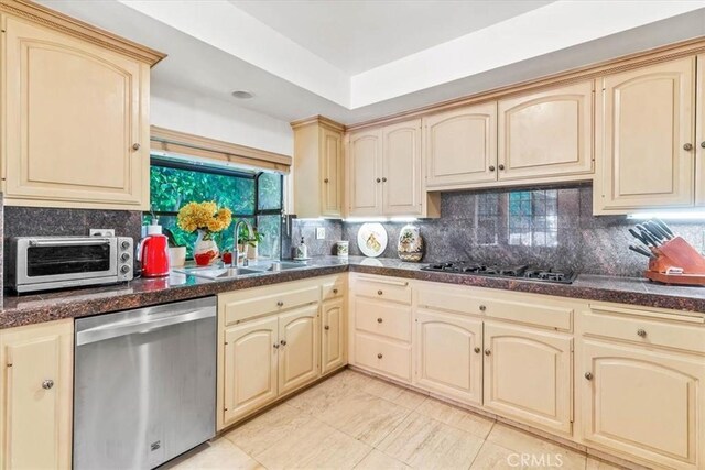 17861 Cathedral Pl, Encino, CA 91316 - kitchen featuring appliances with stainless steel finishes, cream cabinetry, dark countertops, and tasteful backsplash