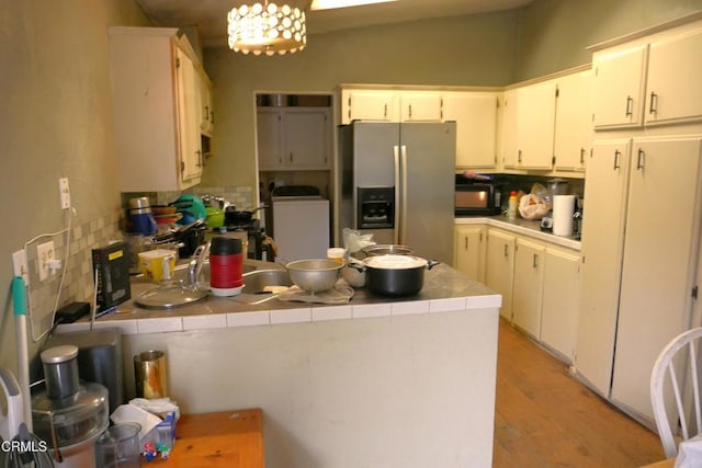 kitchen featuring a peninsula, decorative backsplash, stainless steel fridge with ice dispenser, and tile counters