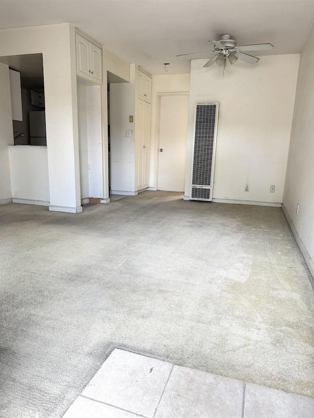 spare room featuring a heating unit, light carpet, a ceiling fan, and baseboards