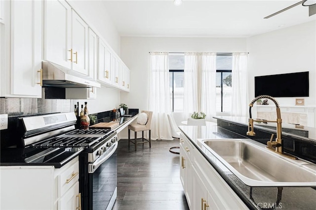 kitchen with under cabinet range hood, dark wood-style flooring, stainless steel gas stove, a sink, and white cabinetry