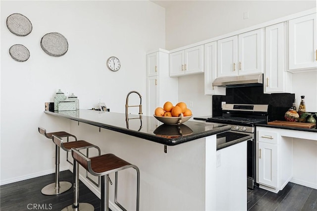kitchen with dark wood-type flooring, a breakfast bar area, under cabinet range hood, gas stove, and white cabinetry