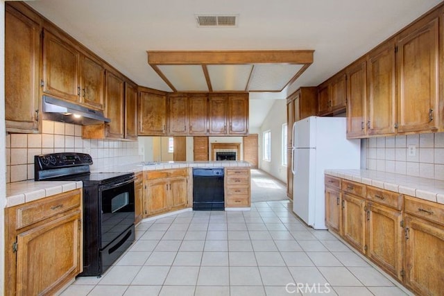 kitchen with under cabinet range hood, visible vents, tile counters, and black appliances