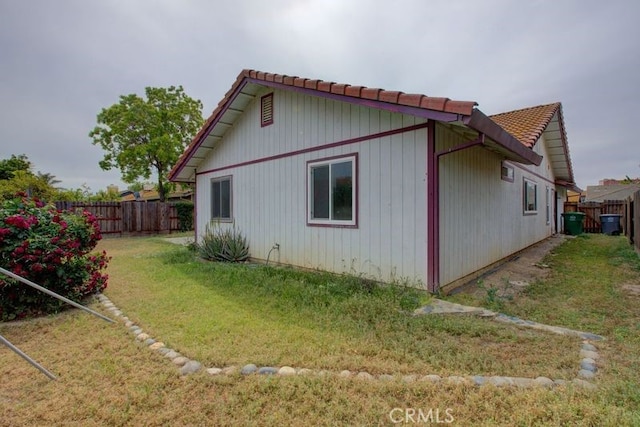 view of side of property with a lawn, a tiled roof, and a fenced backyard