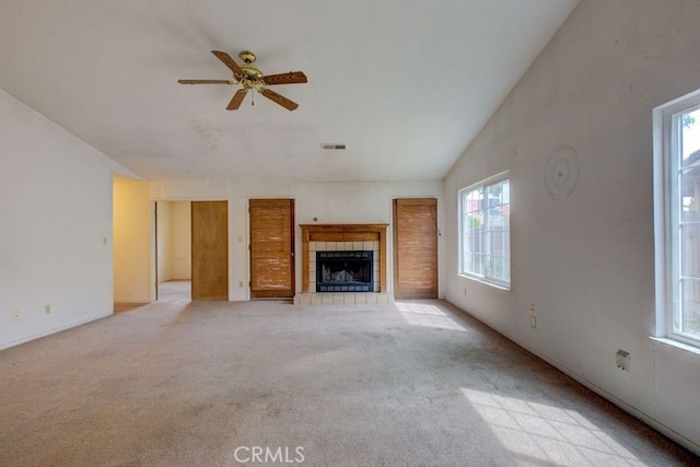 unfurnished living room with a ceiling fan, visible vents, vaulted ceiling, a tile fireplace, and light colored carpet