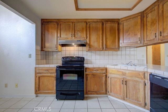kitchen with black appliances, tile countertops, under cabinet range hood, and tasteful backsplash
