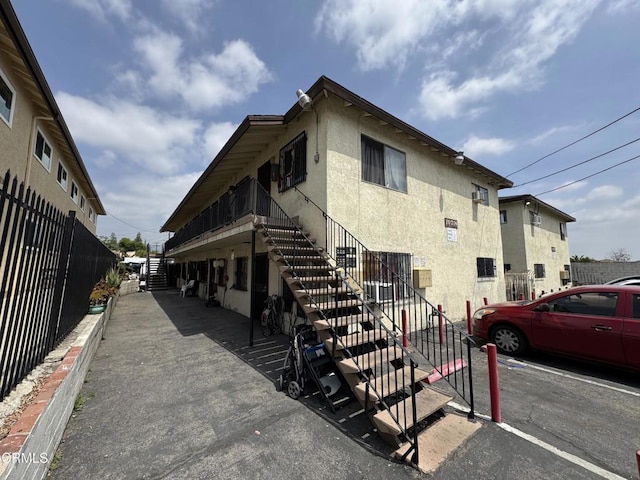 view of side of property featuring uncovered parking, stairs, and stucco siding