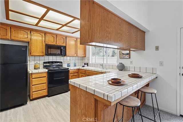 624 Rensselaer Ct, Merced, CA 95348 - kitchen with a peninsula, a breakfast bar, black appliances, tile countertops, and tasteful backsplash