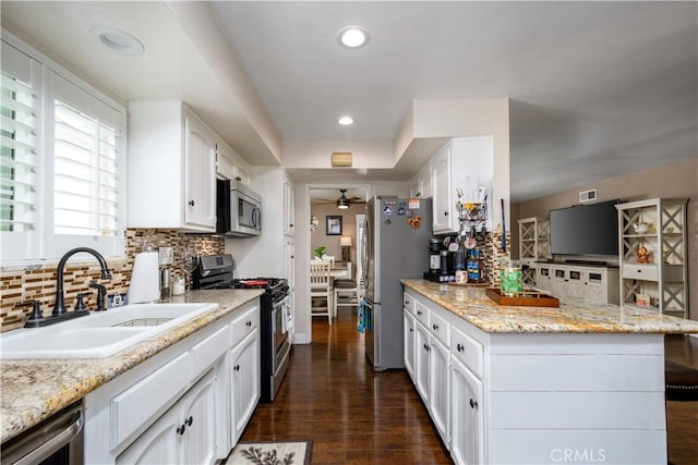 kitchen with a sink, a peninsula, backsplash, white cabinets, and appliances with stainless steel finishes
