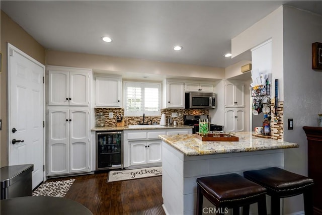 kitchen with beverage cooler, dark wood finished floors, a sink, white cabinetry, and appliances with stainless steel finishes