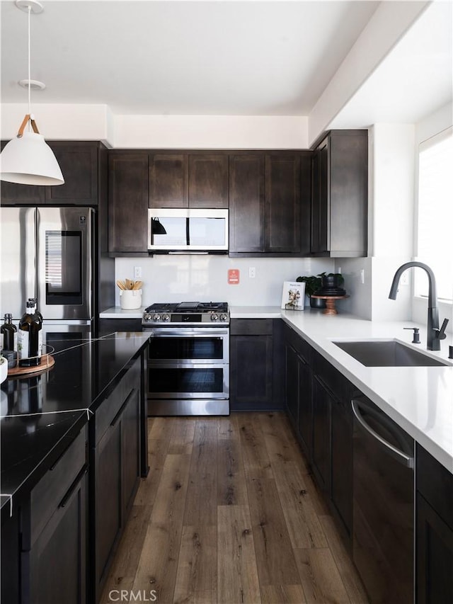 kitchen with a sink, stainless steel appliances, dark brown cabinetry, dark wood-style flooring, and decorative light fixtures