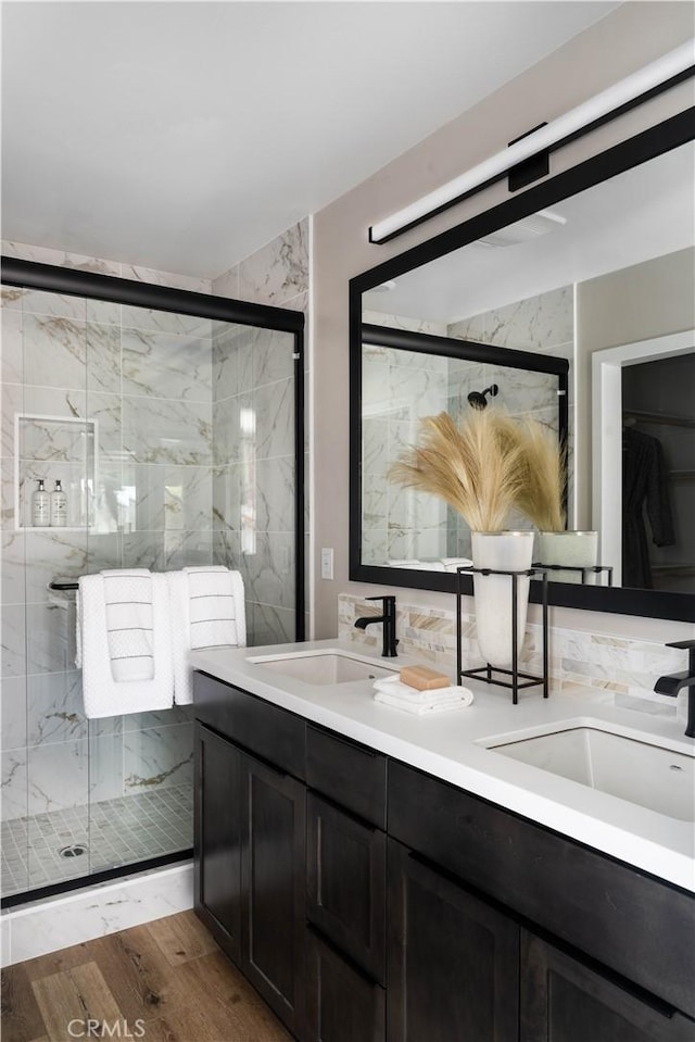 full bath with double vanity, wood finished floors, a stall shower, and a sink