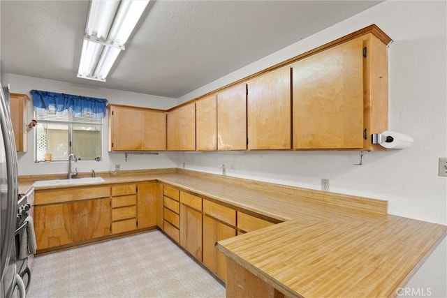 kitchen with light floors, a textured ceiling, a sink, a peninsula, and light countertops