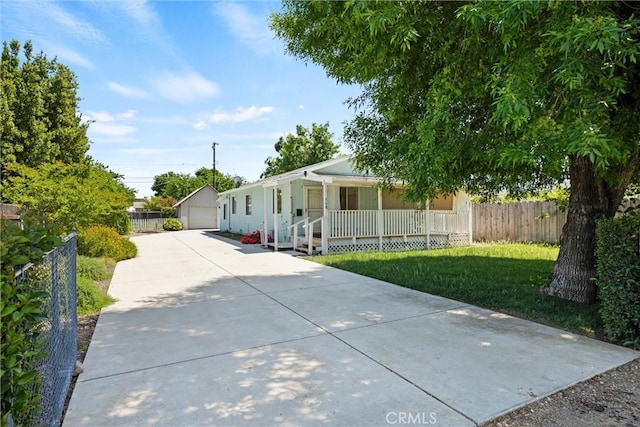 view of front of property with covered porch, fence, a detached garage, an outbuilding, and a front yard