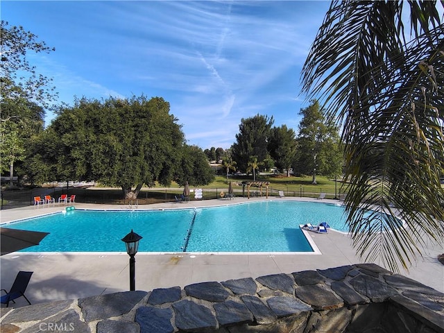 community pool with fence, view of wooded area, and a patio area