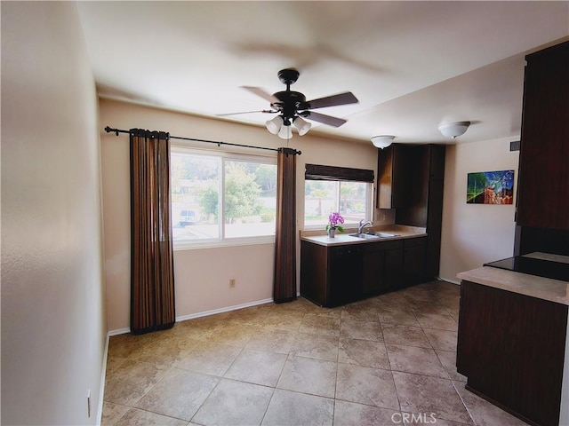 kitchen with a sink, ceiling fan, light countertops, baseboards, and dark brown cabinets