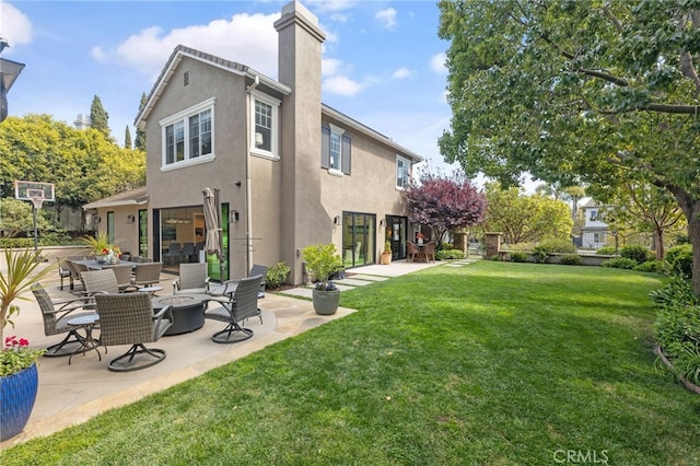 rear view of house with stucco siding, a chimney, a patio area, and a lawn