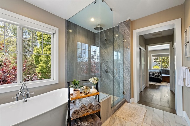 ensuite bathroom featuring plenty of natural light, a stall shower, a soaking tub, and marble look tiles