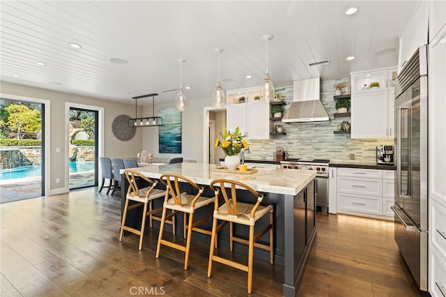 kitchen featuring high end appliances, wall chimney exhaust hood, a kitchen island, white cabinetry, and recessed lighting