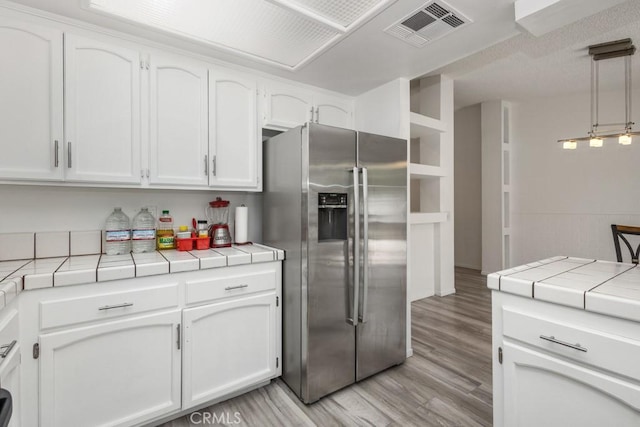 25283 Menominee Ct, Moreno Valley, CA 92553 - kitchen with light wood finished floors, tile counters, stainless steel refrigerator with ice dispenser, white cabinetry, and visible vents