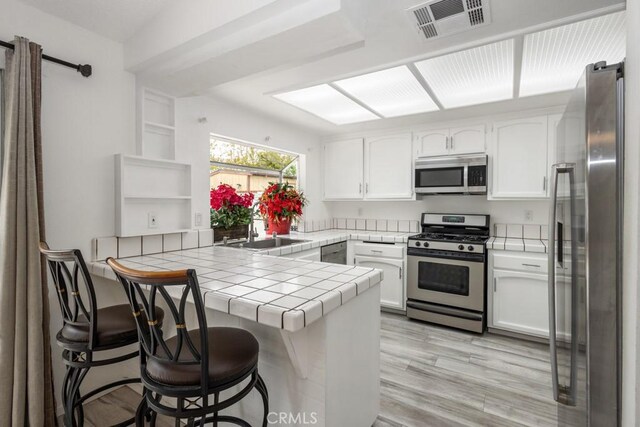 25283 Menominee Ct, Moreno Valley, CA 92553 - kitchen featuring a peninsula, visible vents, tile counters, white cabinets, and appliances with stainless steel finishes
