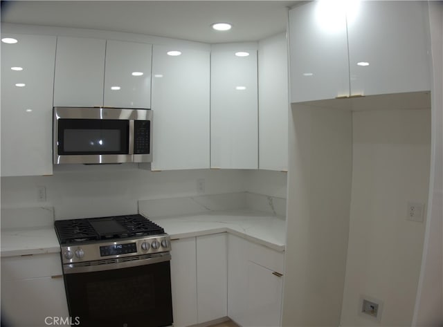 kitchen with light stone countertops, white cabinetry, modern cabinets, and appliances with stainless steel finishes