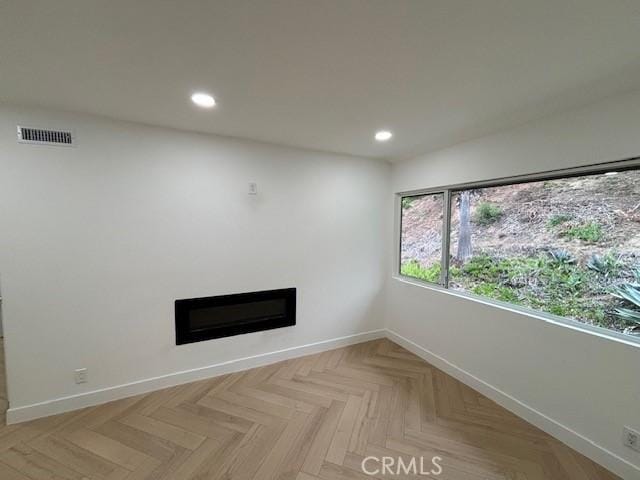 spare room featuring baseboards, recessed lighting, a glass covered fireplace, and visible vents