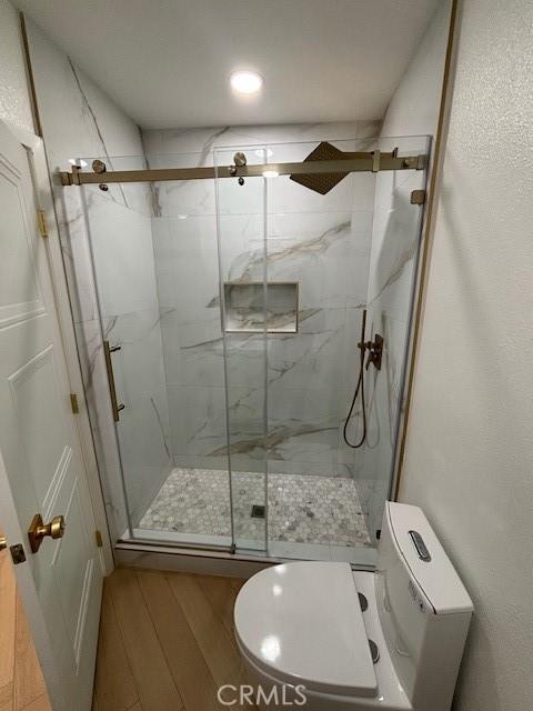bathroom featuring toilet, a marble finish shower, and wood finished floors