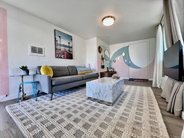 living room with a textured wall, baseboards, visible vents, and wood finished floors