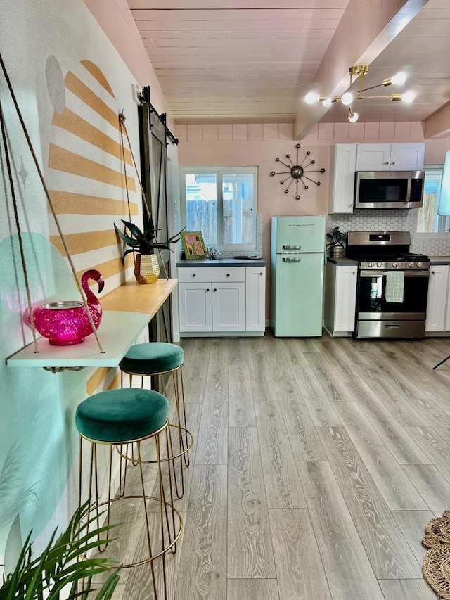 kitchen with white cabinets, a barn door, stainless steel appliances, and light wood finished floors