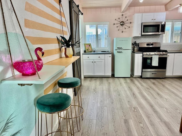 kitchen featuring light wood-style flooring, decorative backsplash, beamed ceiling, stainless steel appliances, and white cabinets