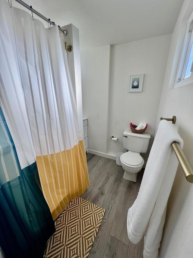 bathroom with toilet, curtained shower, wood finished floors, and baseboards
