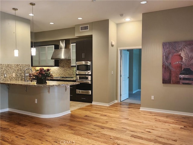 kitchen featuring wall chimney exhaust hood, stainless steel appliances, a kitchen breakfast bar, visible vents, and light wood-style floors