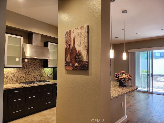 21 Gramercy Unit 115, Irvine, CA 92612 - kitchen featuring wall chimney range hood, decorative backsplash, stainless steel gas stovetop, glass insert cabinets, and dark cabinets