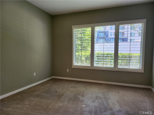 empty room with baseboards, dark carpet, and a wealth of natural light