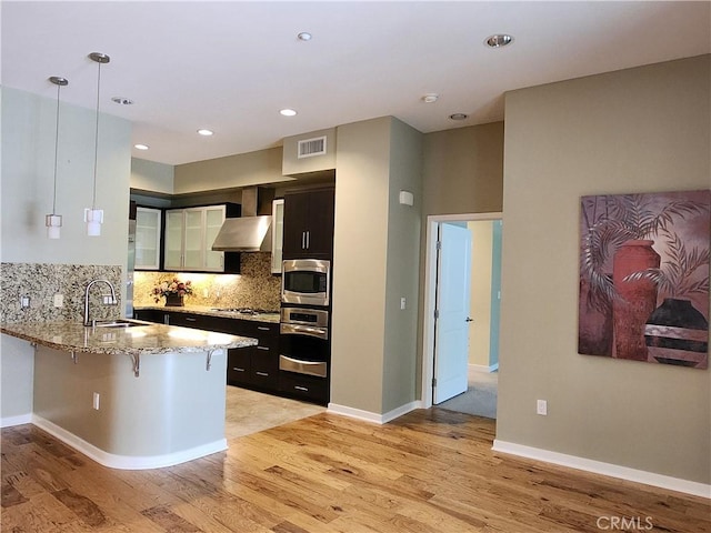kitchen with a sink, a peninsula, a kitchen breakfast bar, visible vents, and dark cabinets