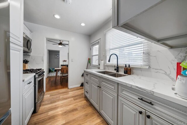 kitchen with light wood-style flooring, a ceiling fan, a sink, stainless steel appliances, and decorative backsplash