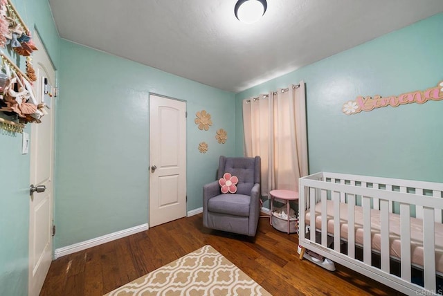 bedroom featuring baseboards, a nursery area, and wood finished floors