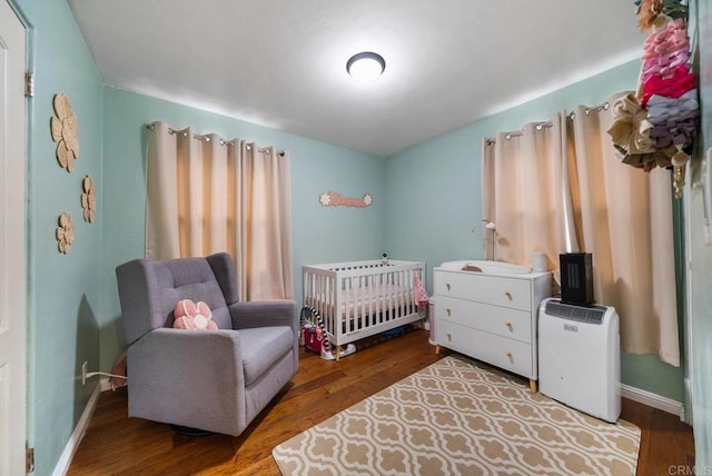 bedroom featuring baseboards, a nursery area, and wood finished floors