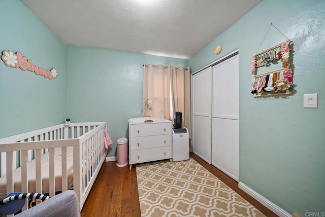 bedroom featuring a closet, a nursery area, baseboards, and wood finished floors