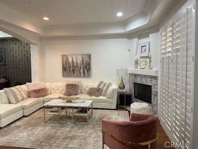 living room with a tray ceiling, wood finished floors, a fireplace, and ornamental molding