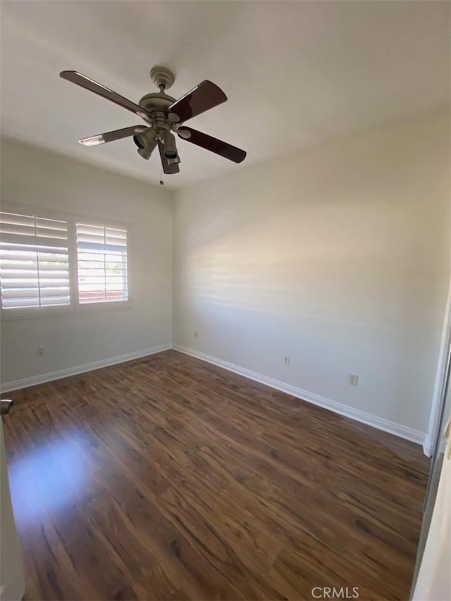 spare room featuring a ceiling fan, baseboards, and dark wood-type flooring
