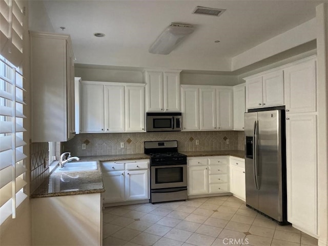 kitchen featuring dark stone countertops, a sink, stainless steel appliances, white cabinets, and visible vents