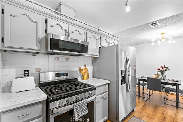 11348 Ramona Ave, Pomona, CA 91766 - kitchen featuring visible vents, a chandelier, backsplash, light wood-style floors, and appliances with stainless steel finishes