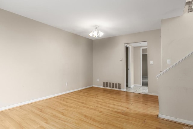 empty room featuring a notable chandelier, light wood-style flooring, baseboards, visible vents, and stairs