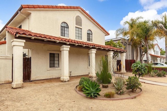 rear view of property featuring fence, stucco siding, and a tiled roof