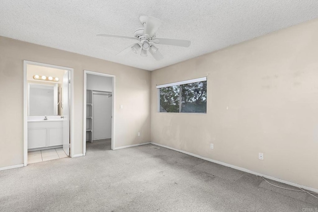 unfurnished bedroom featuring a textured ceiling, carpet, baseboards, connected bathroom, and a walk in closet