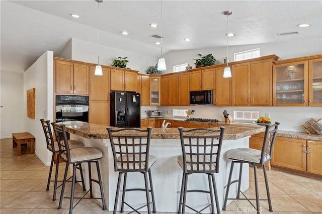 51565 Avenida Carranza Ln, Quinta, CA 92253 - kitchen featuring black appliances, light tile patterned floors, brown cabinetry, a kitchen breakfast bar, and a kitchen island with sink