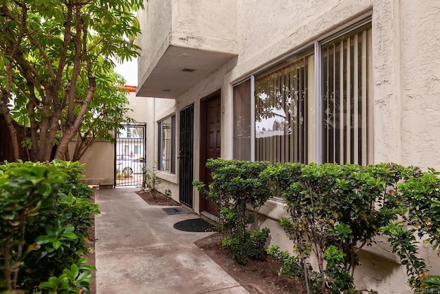 view of exterior entry with a gate, stucco siding, and visible vents